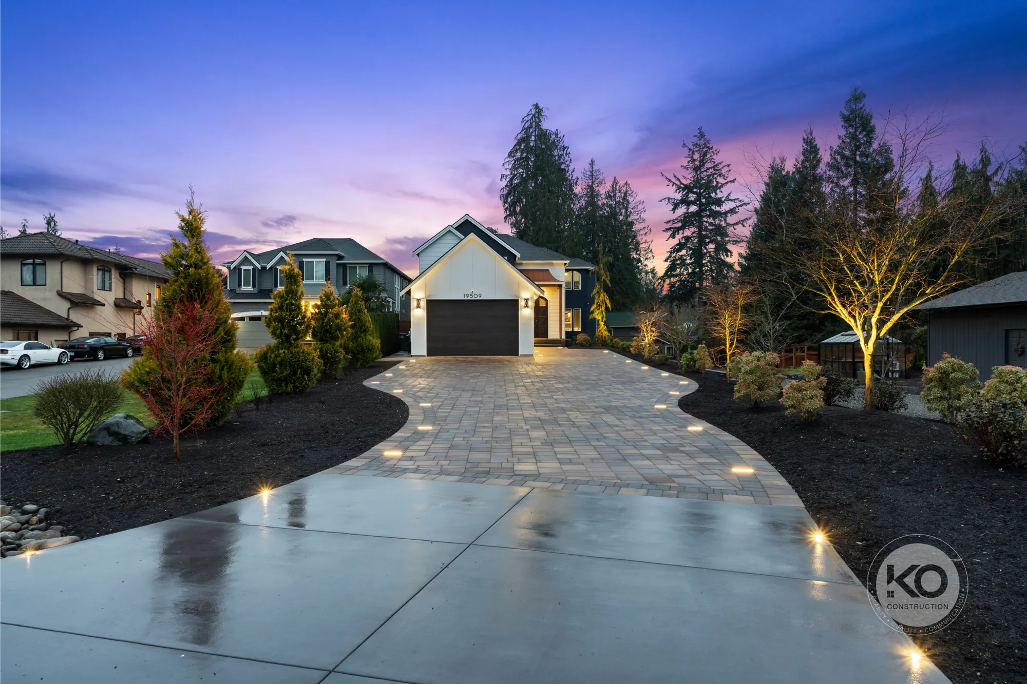 A KO Construction home at dusk with a lit paver driveway