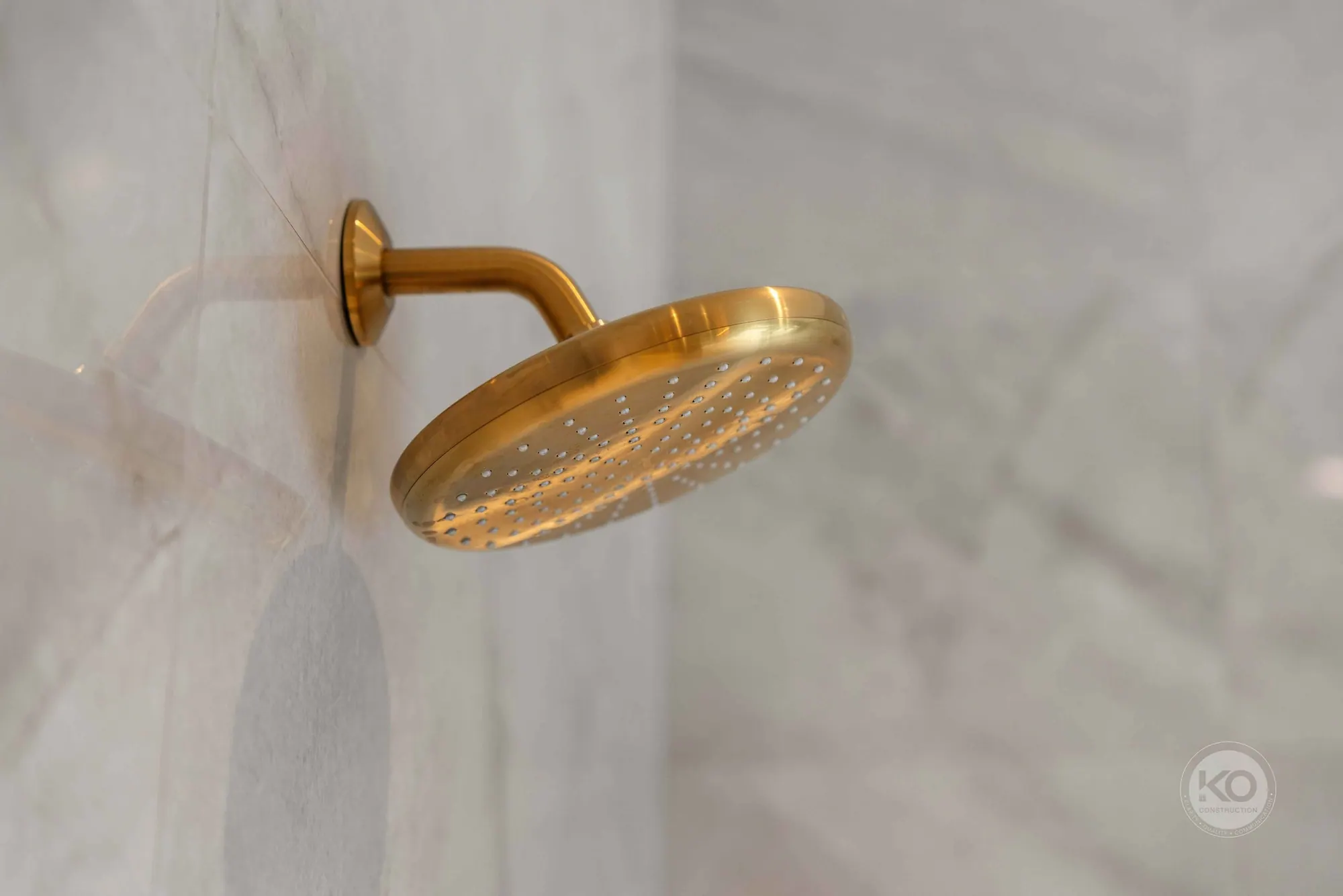 Brushed brass rain shower head on marble tile